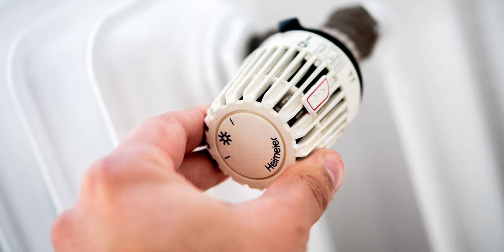 Ein Mann dreht in einer Wohnung am Thermostat einer Heizung.
