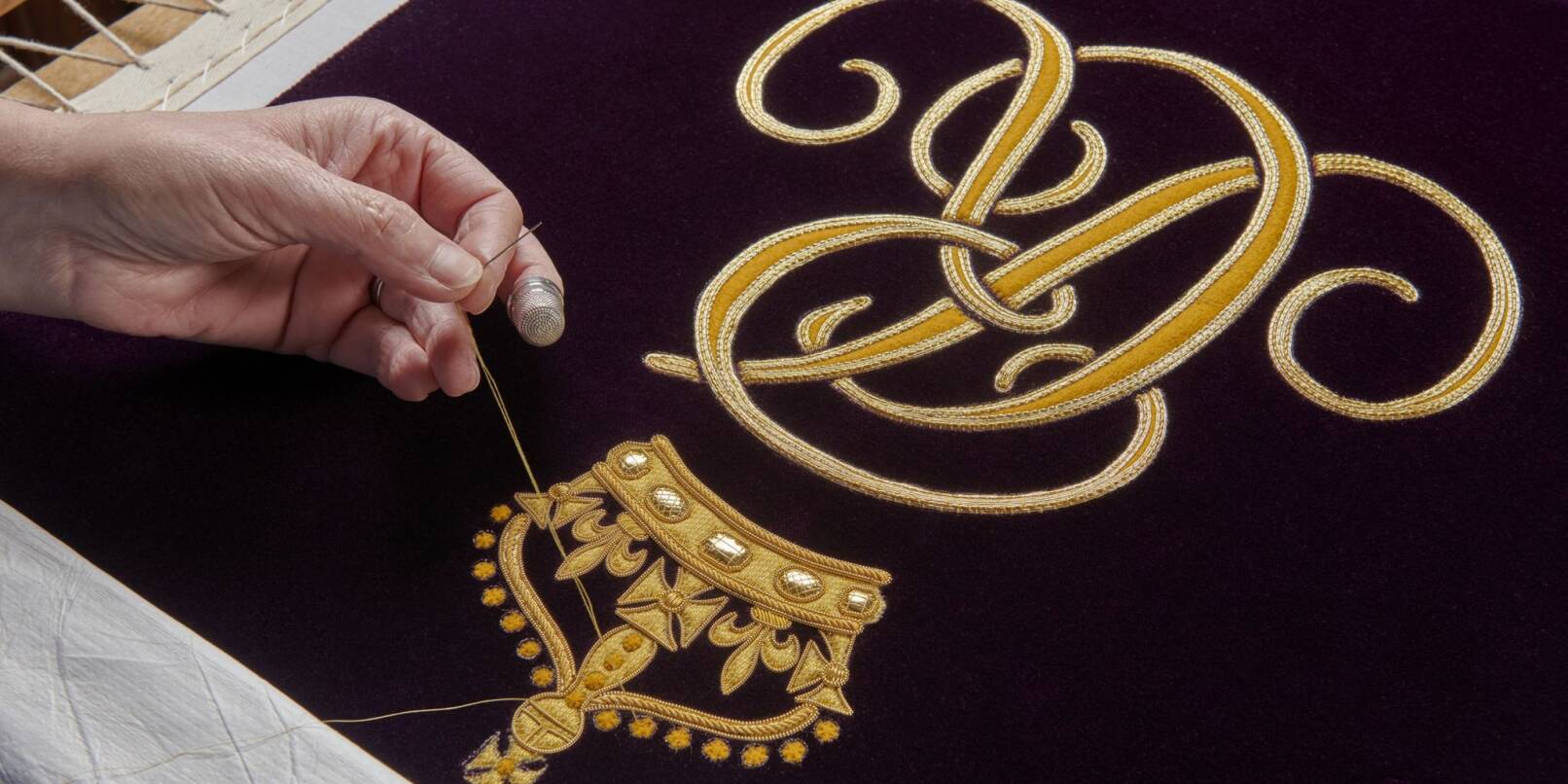 Ein Mitglied der Royal School of Needlework stickt den Schriftzug von Queen Camilla von Hand auf deren Robe.