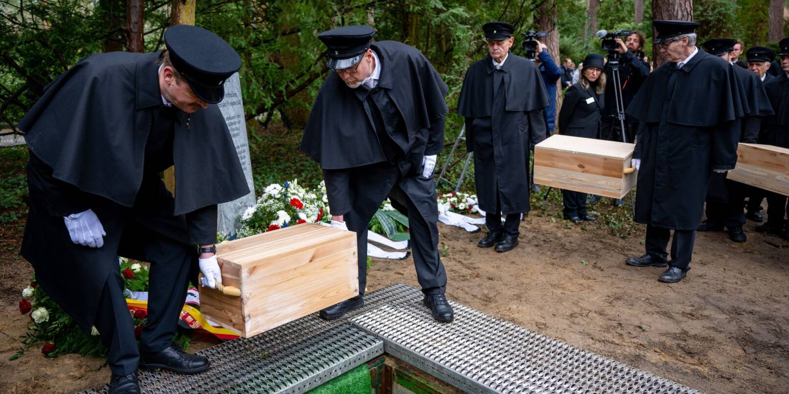 Die Gebeinekisten mit menschlichen Knochen werden nach der Trauerfeier in ein Grab auf dem Waldfriedhof Berlin-Dahlem hinabgelassen.