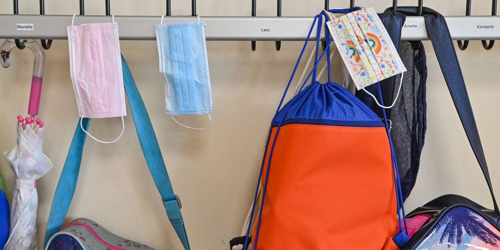 Medizinische Masken und Schultaschen hängen in einer Schulgarderobe.